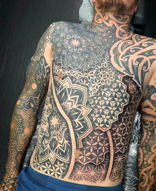 man with chest and stomach covered in tribal and mandala tattoos